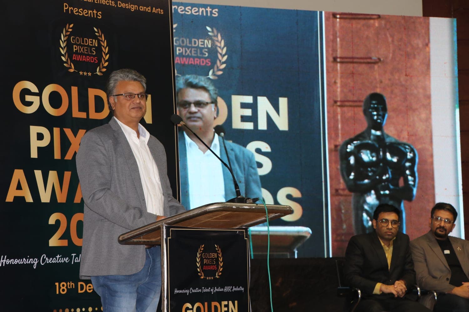 Speaker at the podium on the Golden Pixels Awards stage with the screen behind