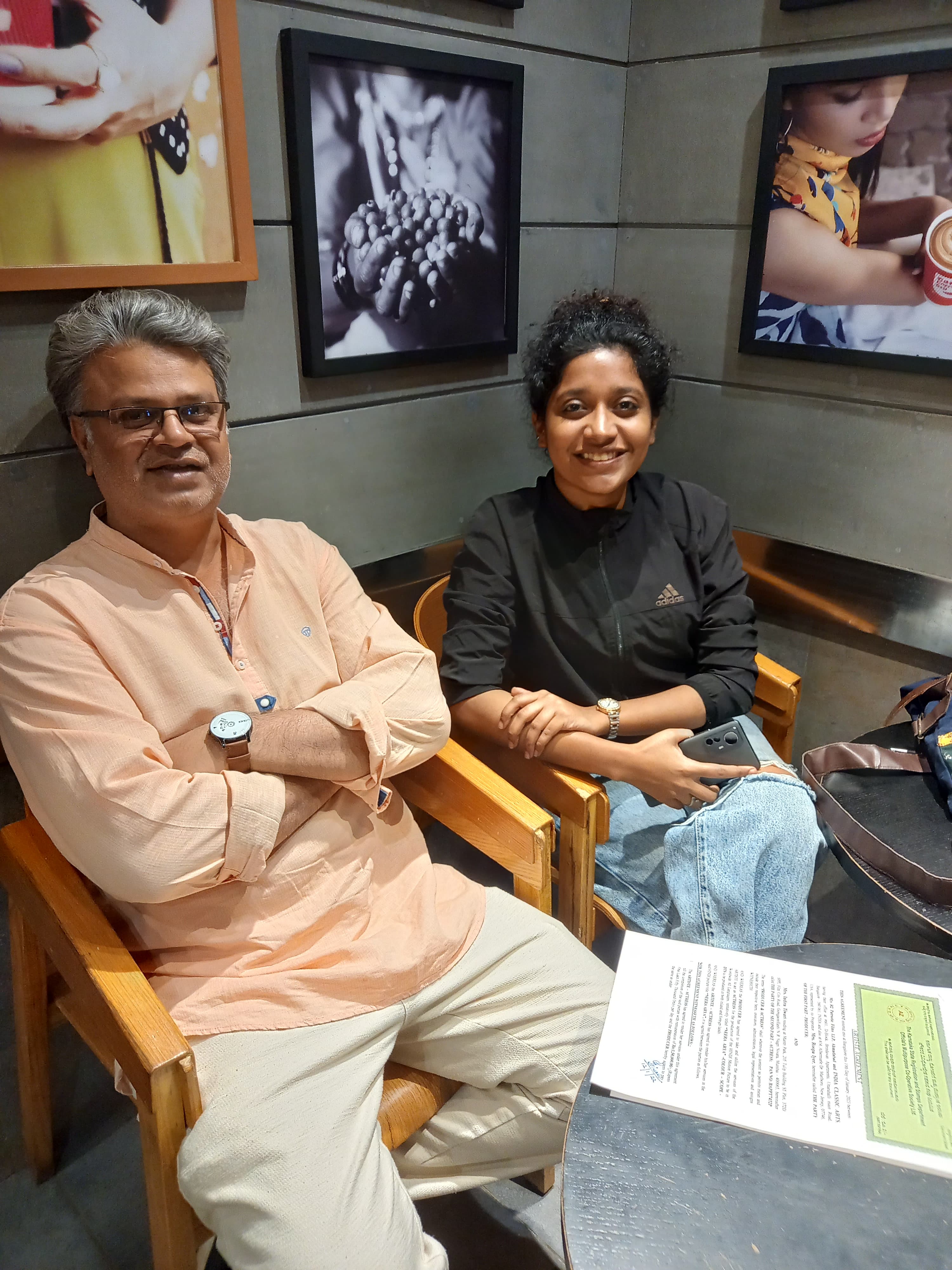 Producer and actor seated in director's chairs beside a signed artiste agreement