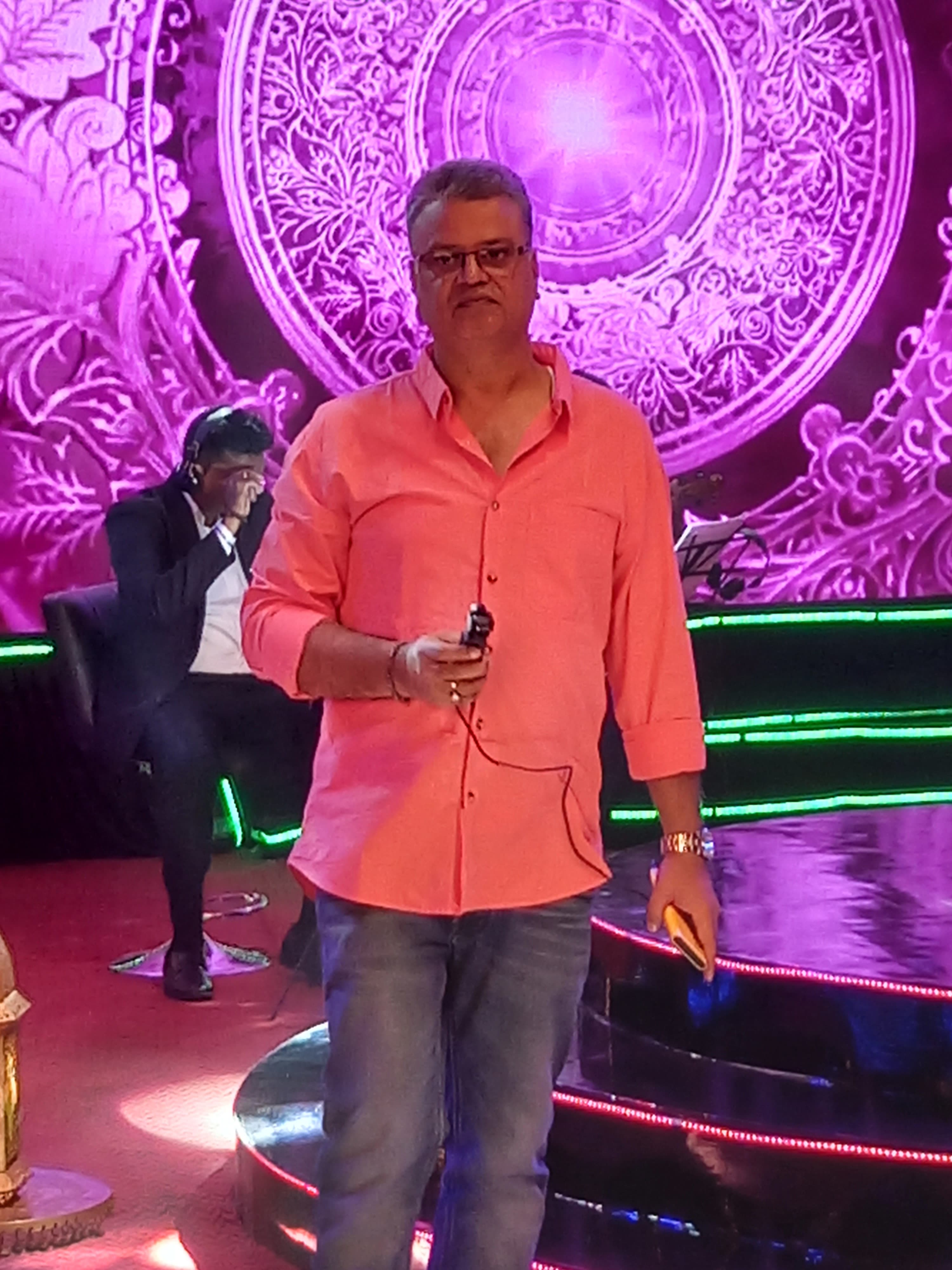 Host with a microphone on a brightly lit decorated stage during a live show
